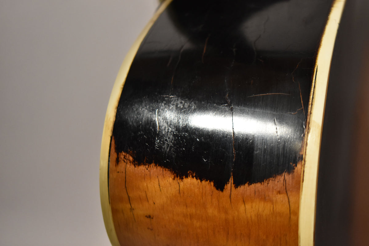 Close-up of the guitar's side, showing heavy black finish wear and checking revealing the natural wood underneath, with cream binding.