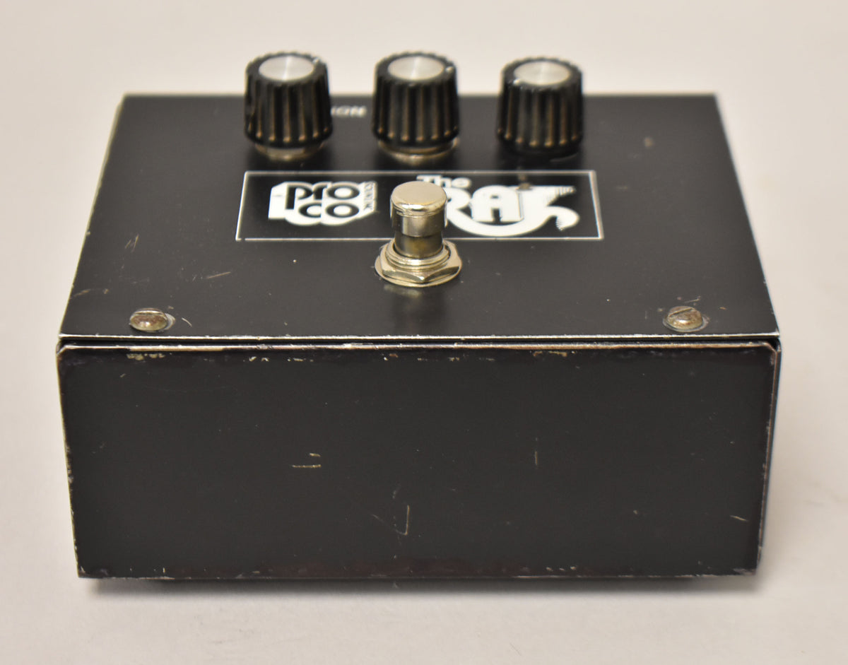 Black rectangular pedal with three black ridged knobs, a silver footswitch, and visible scratches and paint chips.