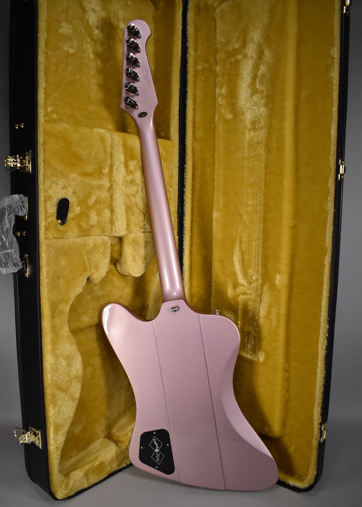 The back of a heather poly Firebird guitar, neck and headstock visible, rests in a plush yellow-lined black hard case.