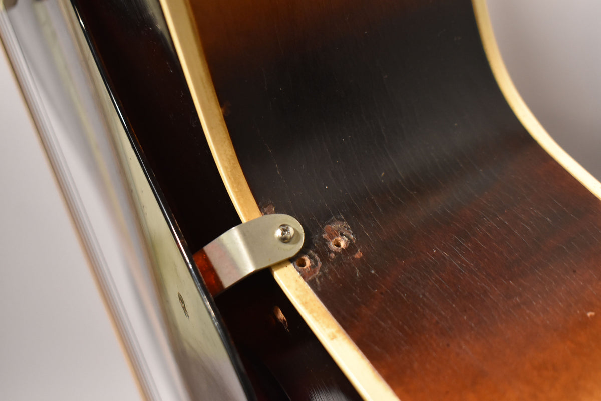 Close-up of the guitar's sunburst body, showing a metal bracket with a screw and two empty screw holes, plus finish checking.