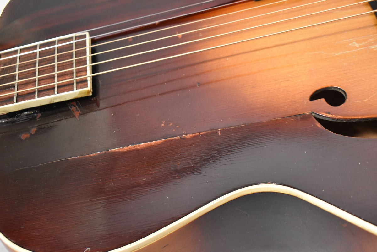 Close-up of the sunburst archtop's lower bout, showing a white bound body, f-hole, and heavy finish wear near the fretboard.