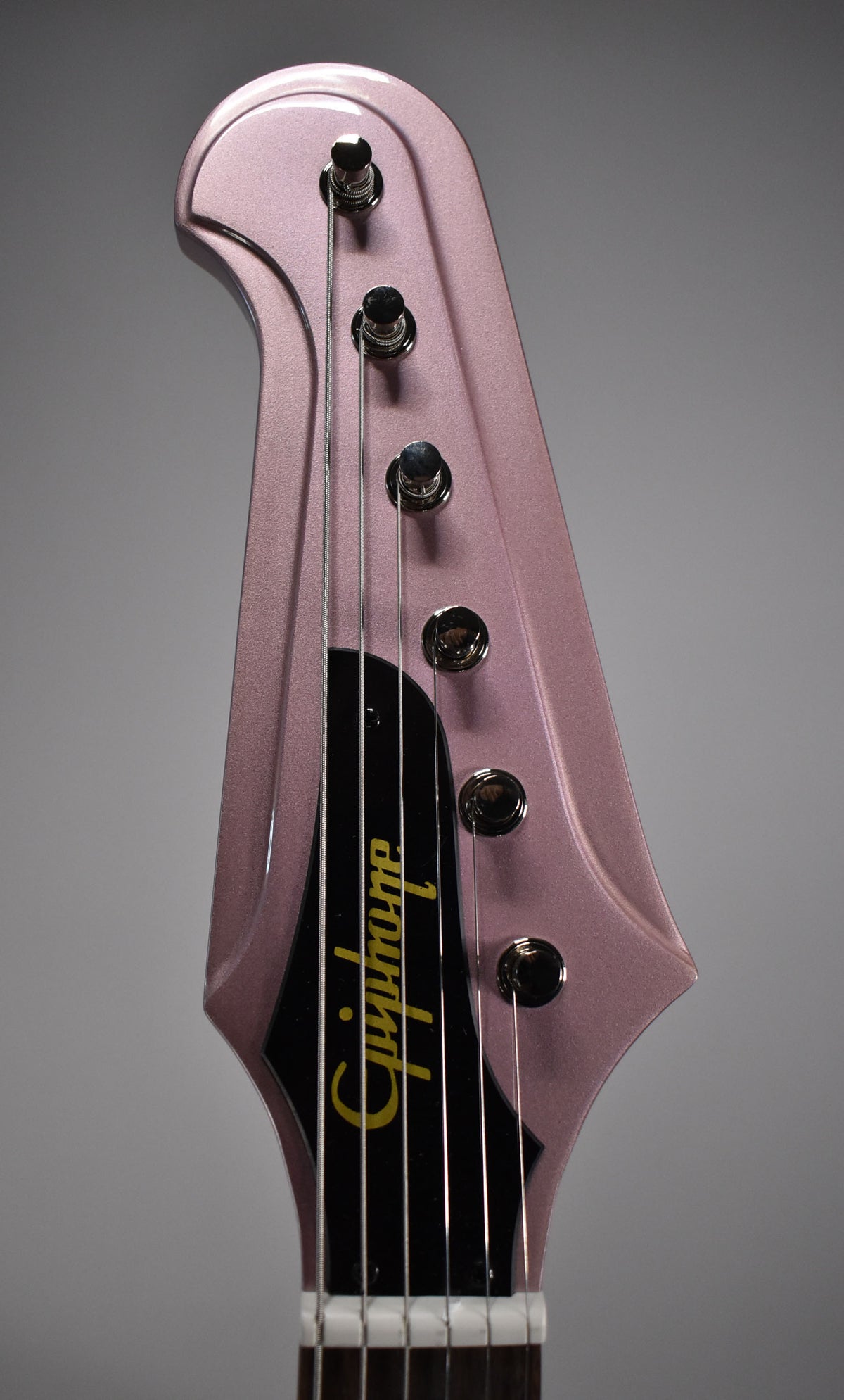 Close-up of a metallic pink guitar headstock with six chrome tuners, black truss rod cover, and "Epiphone" in gold script.