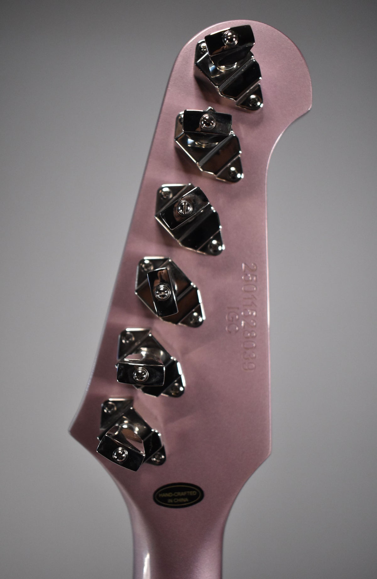 The back of a heather poly headstock with six chrome tuners and a visible serial number.