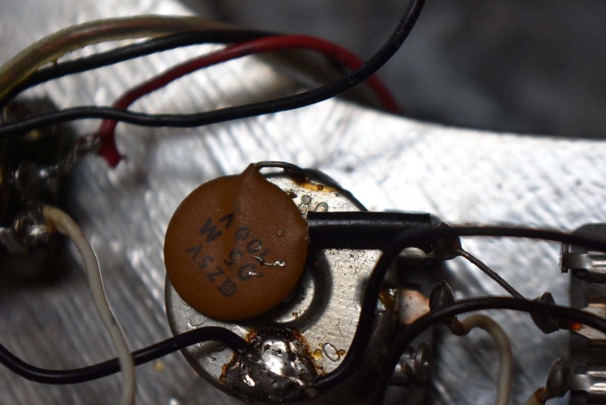 Close-up of internal wiring, showing a brown disc capacitor soldered to a silver pot, surrounded by black, red, and white wires.