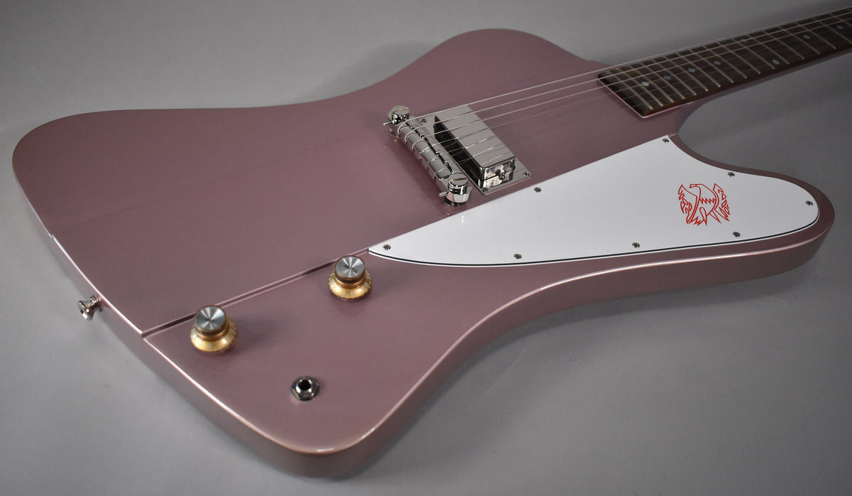 The Firebird's heather poly body is angled from the lower right, showing two gold-capped knobs and a white pickguard with a red bird graphic.