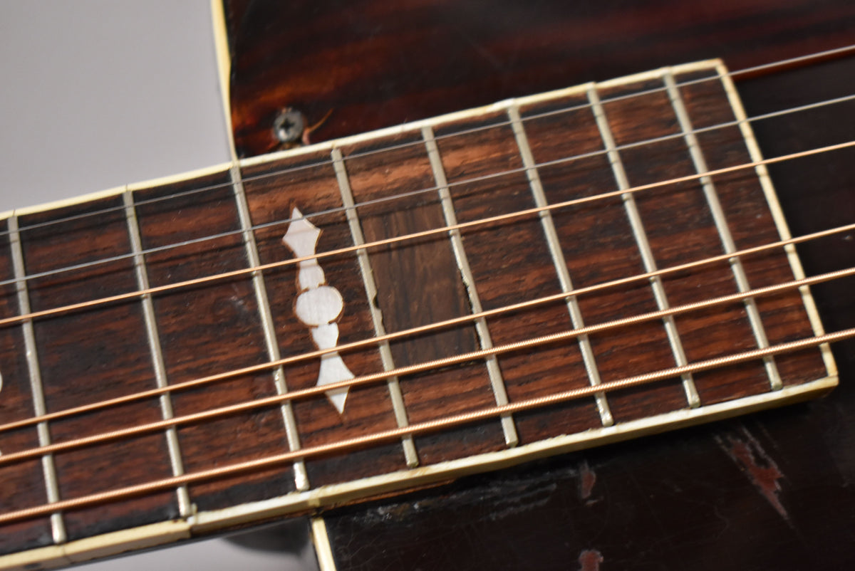 Close-up of the dark brown fretboard with ornate mother-of-pearl inlays, showing wear and a screw visible where the neck meets the body.