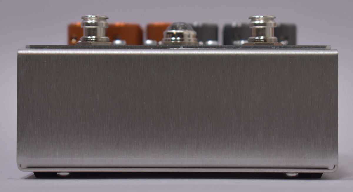 The brushed silver pedal is viewed from the side, revealing two silver footswitches and a clear dome knob on top.