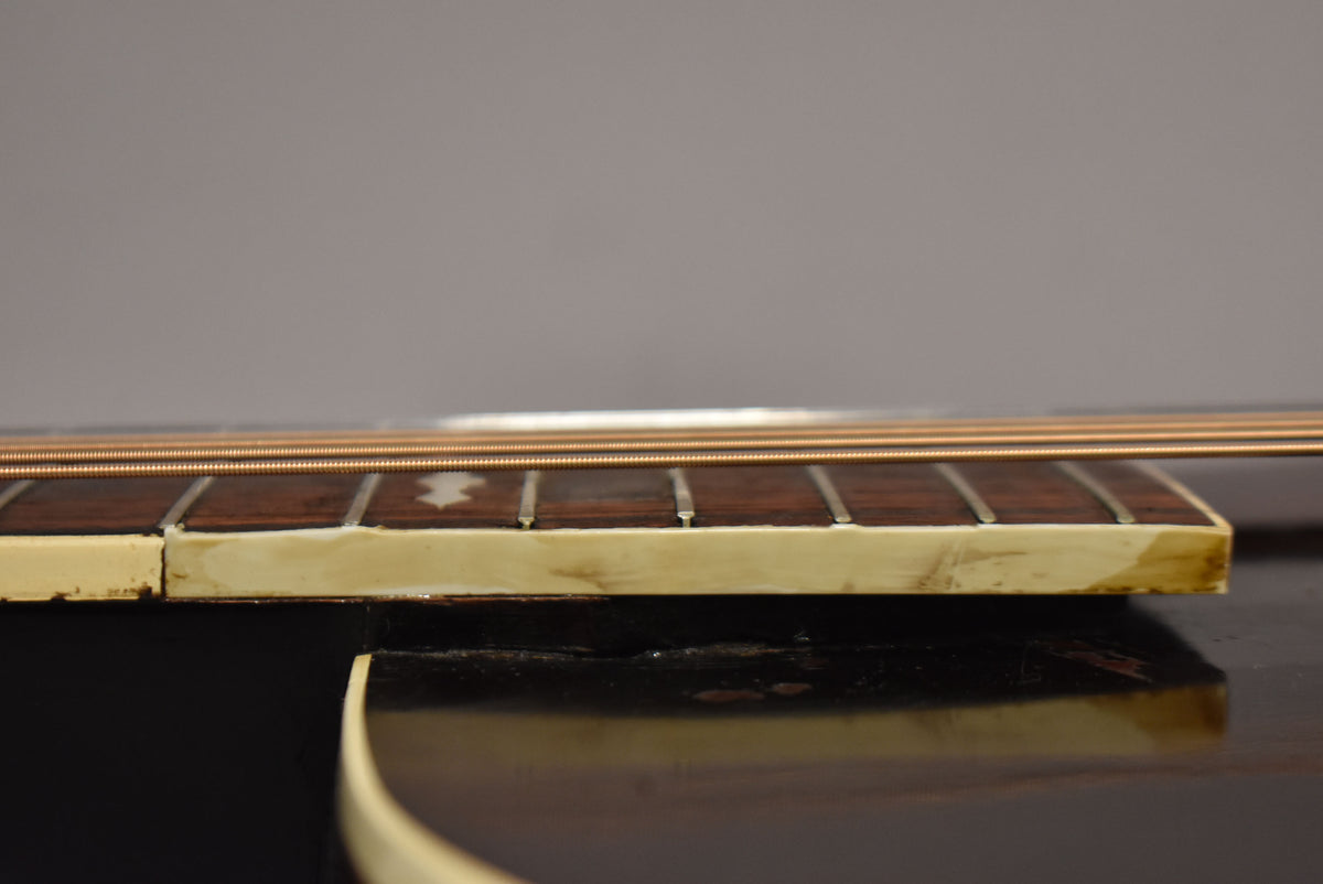 Close-up, side view of the guitar's dark brown fretboard with cream binding, showing light wear and a star inlay.