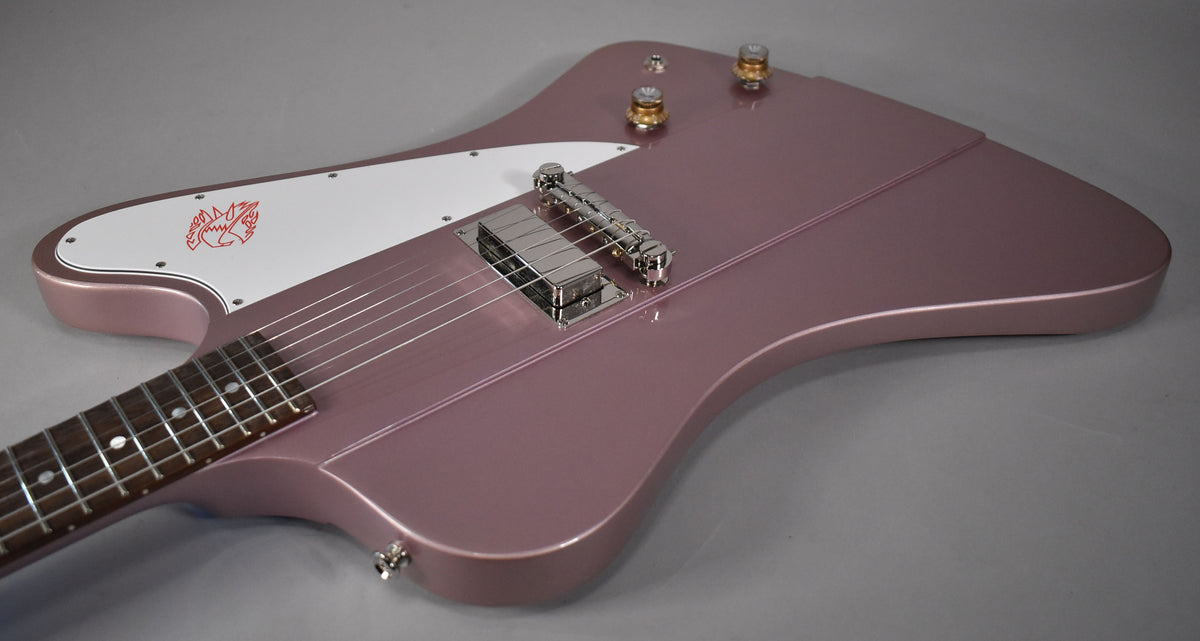 The Firebird's heather poly body is angled, showing the white pickguard with red bird graphic, chrome bridge, and two gold knobs.