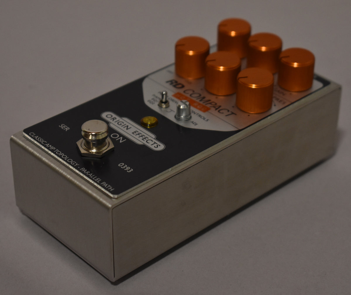 Angled view of a silver pedal with a black faceplate, six orange knobs, a silver footswitch, and two small toggle switches.