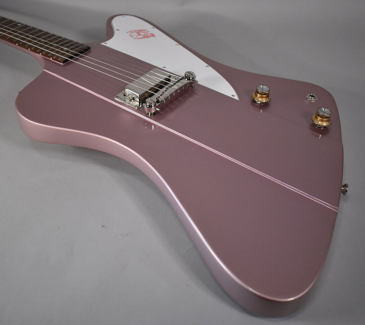 The Firebird's heather poly body, with a white pickguard and chrome hardware, is angled to show the bridge and two gold-capped knobs.