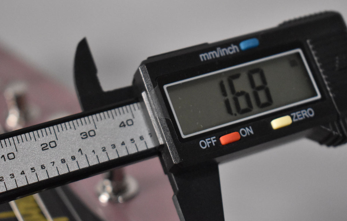 A digital caliper measures the guitar's nut width, displaying "1.68" inches, with the headstock's heather poly finish visible behind it.