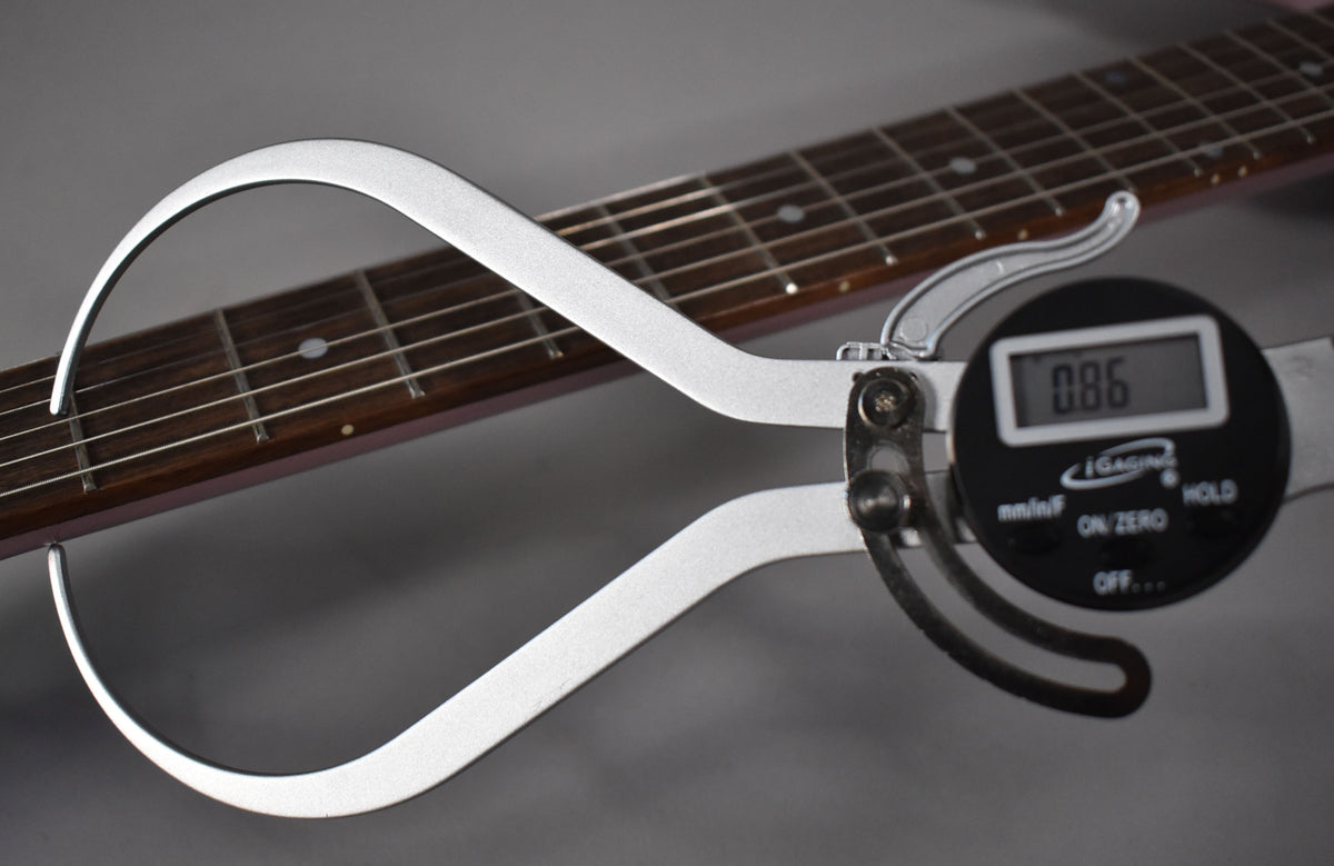 A digital caliper measures the neck thickness of the heather poly Firebird, showing a dark rosewood fretboard with dot inlays.