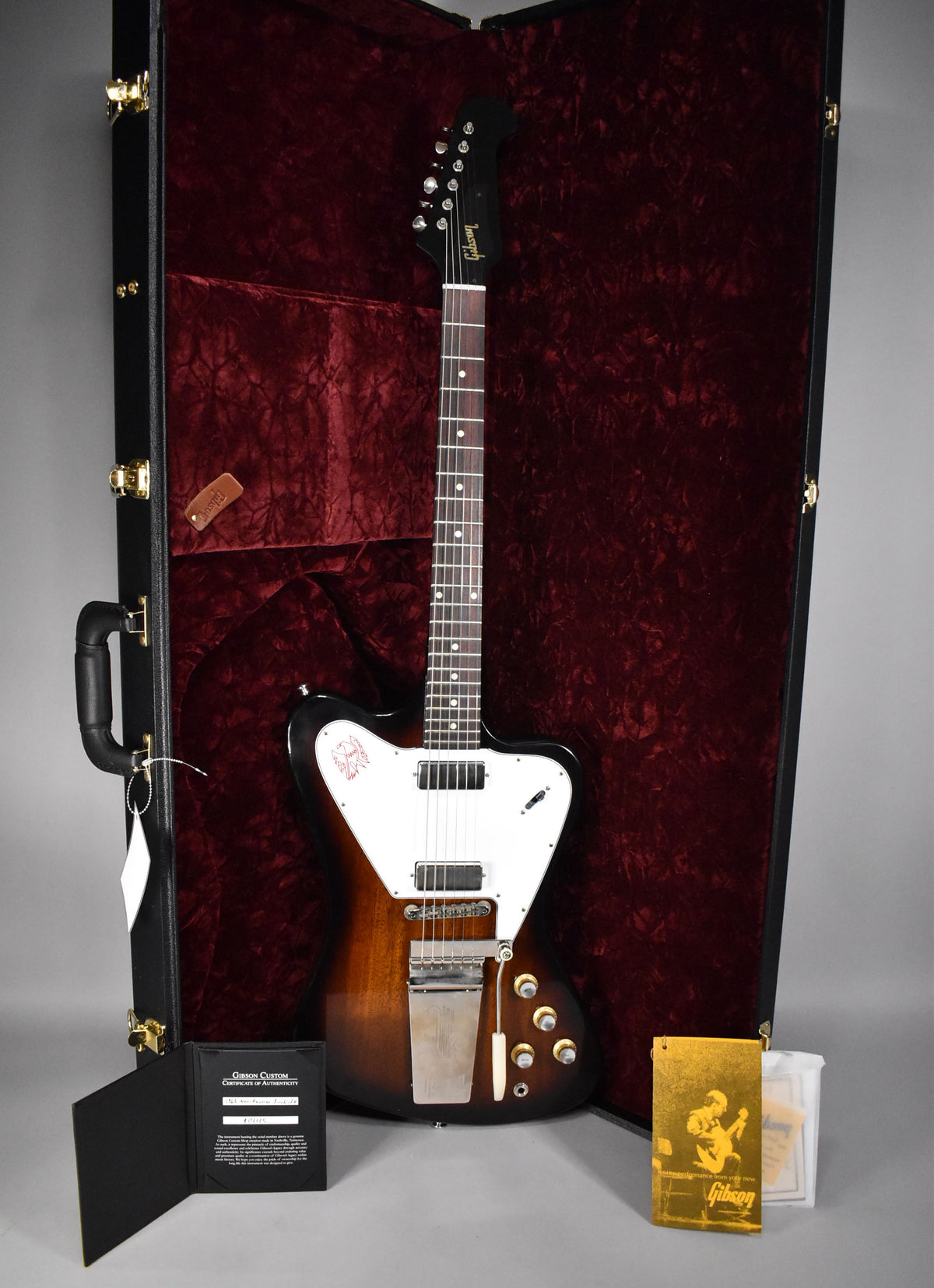 Sunburst Firebird V in an open hard case with red velvet lining, showing its white pickguard, two humbuckers, and vibrato.
