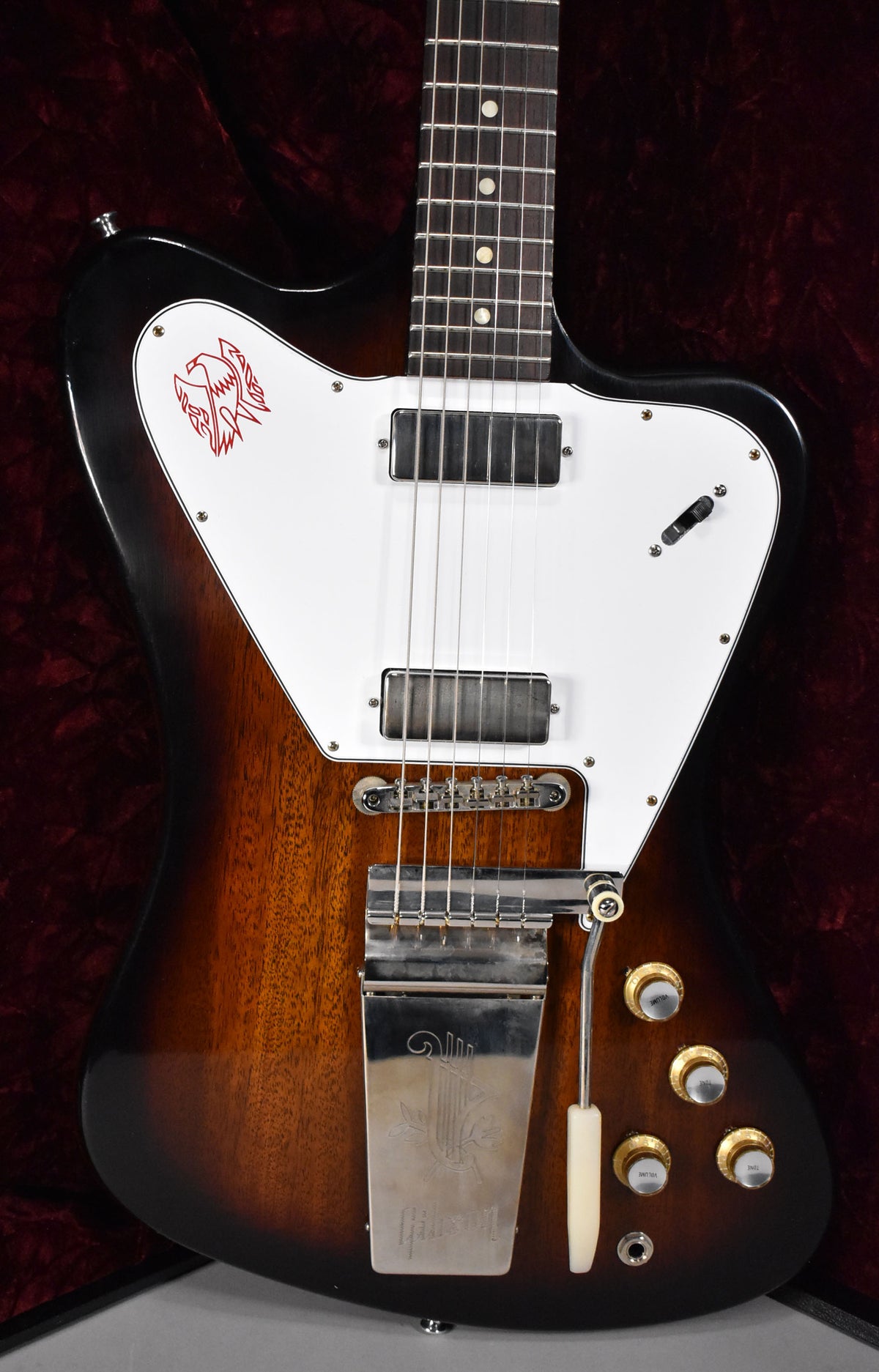 The Firebird's body, with a vintage sunburst finish, is angled to show the white pickguard with a red bird graphic, two humbuckers, and a vibrato tailpiece.