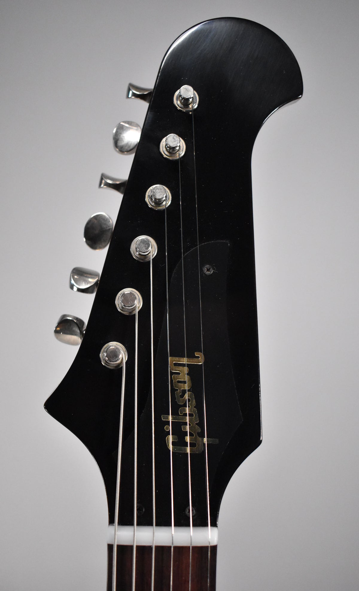 The glossy black headstock, with six chrome tuners on the left, is angled slightly right, showing the gold logo and truss rod cover.