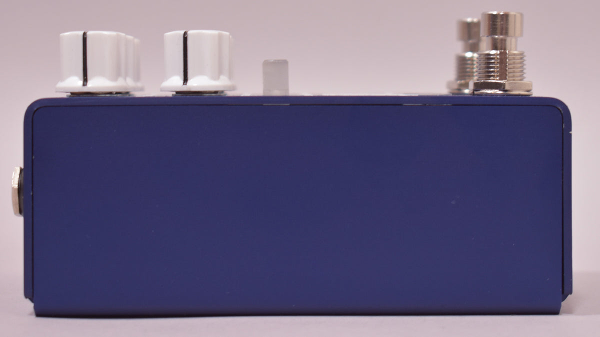 The overdrive pedal is shown from the side, revealing its matte blue finish, two white knobs, a clear LED, and two silver jacks.