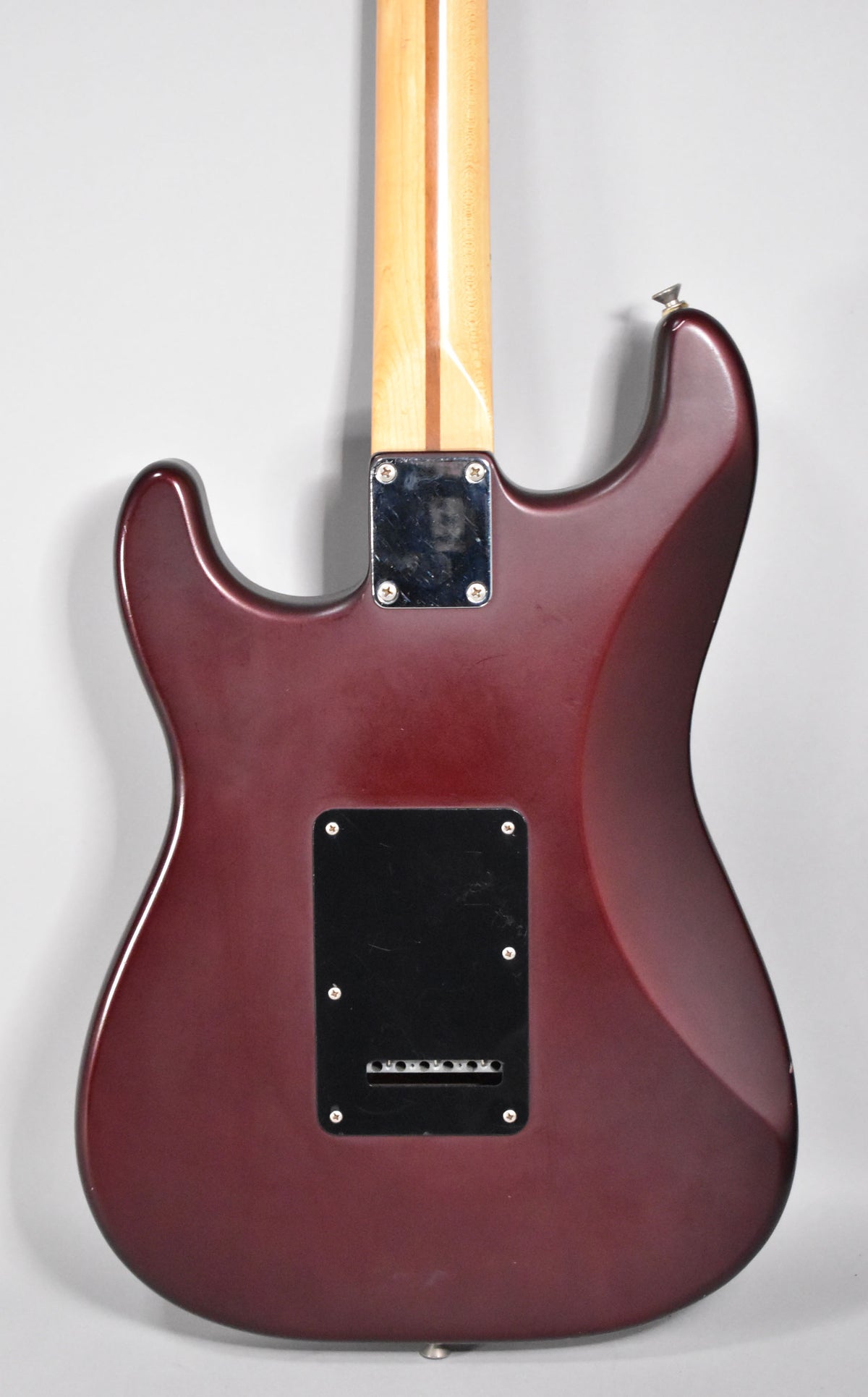 The back of a satin metallic red Stratocaster, showing the neck plate, tremolo cover, and light wear on the body.