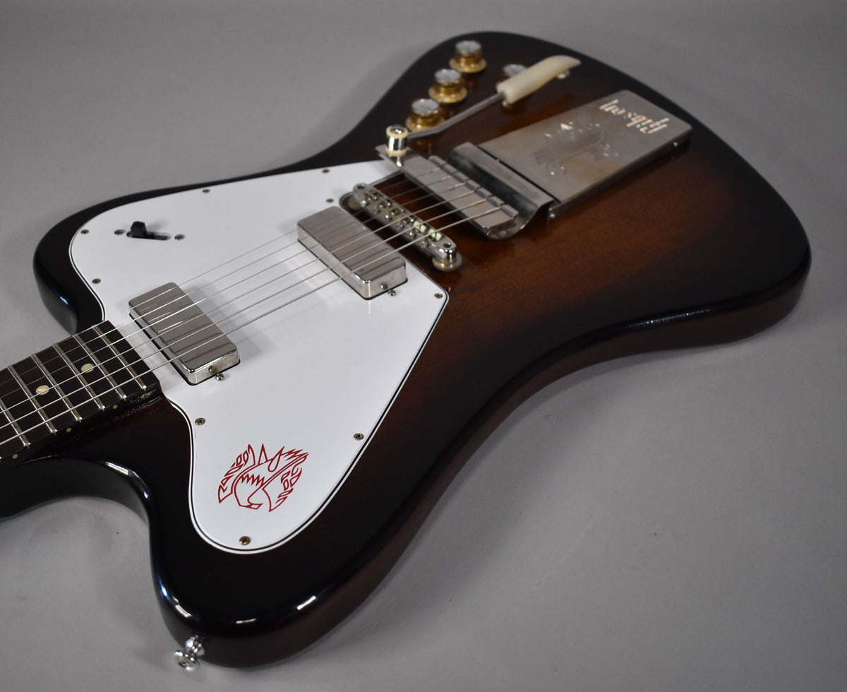 The guitar's body, in vintage sunburst, is angled from the lower left, showing the white pickguard with a red firebird graphic.