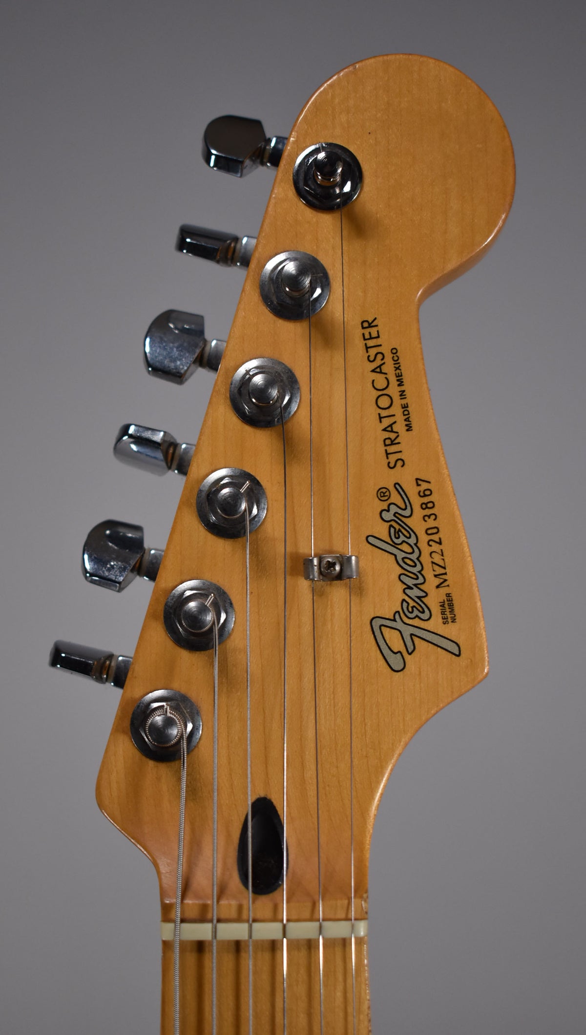 Close-up of the headstock, angled slightly right, showing six chrome tuners, a string tree, and a light maple finish.