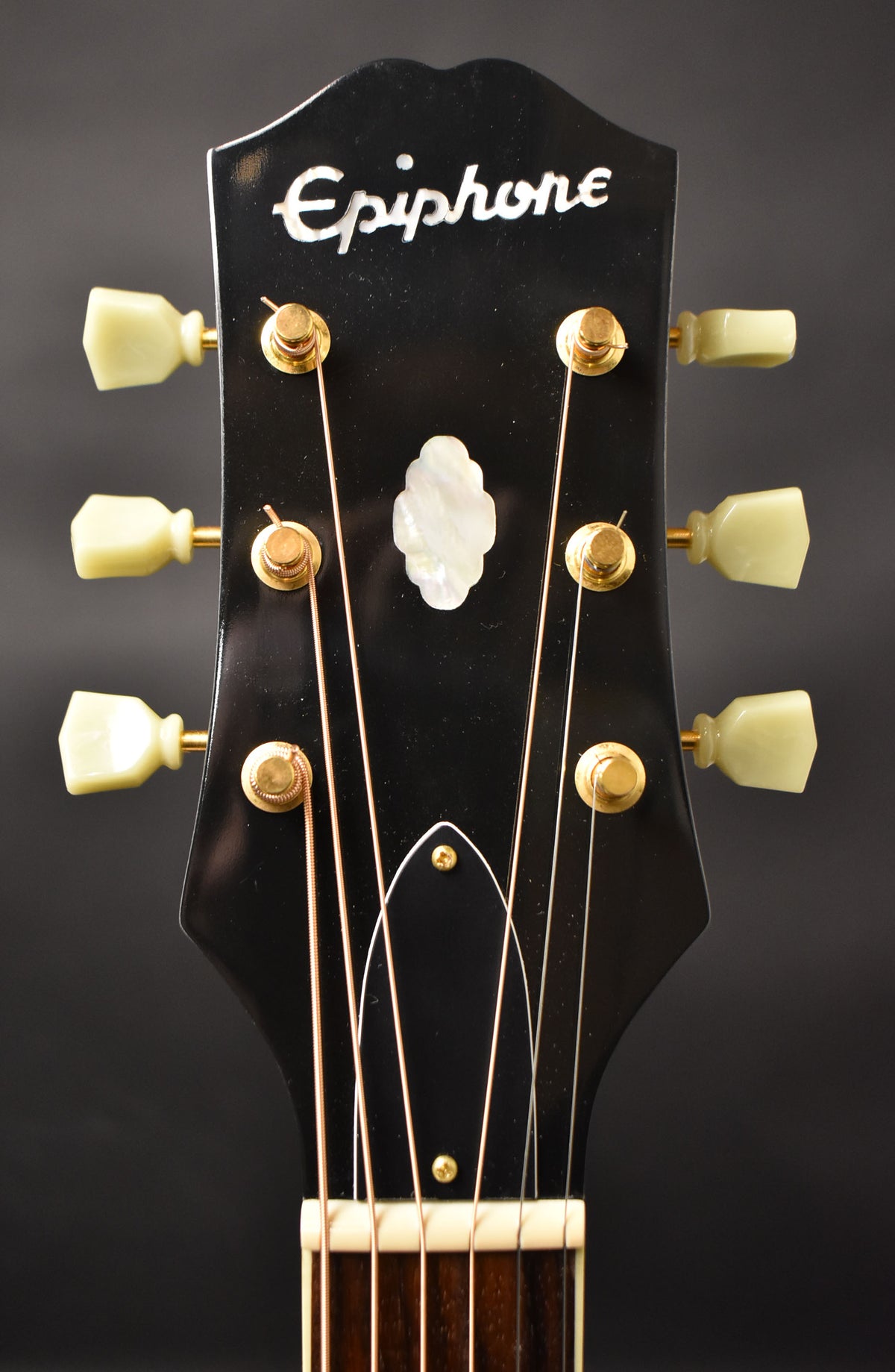 Close-up of the glossy black headstock with cream tuning pegs, gold hardware, and a mother-of-pearl inlay.