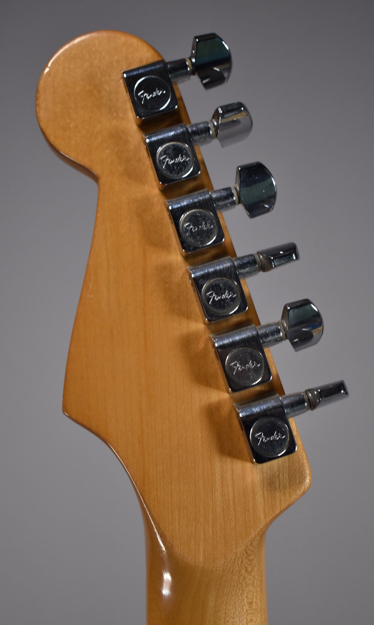 Rear view of the guitar's headstock and neck, showing six chrome tuners on a light wood finish, with some minor wear on the wood.