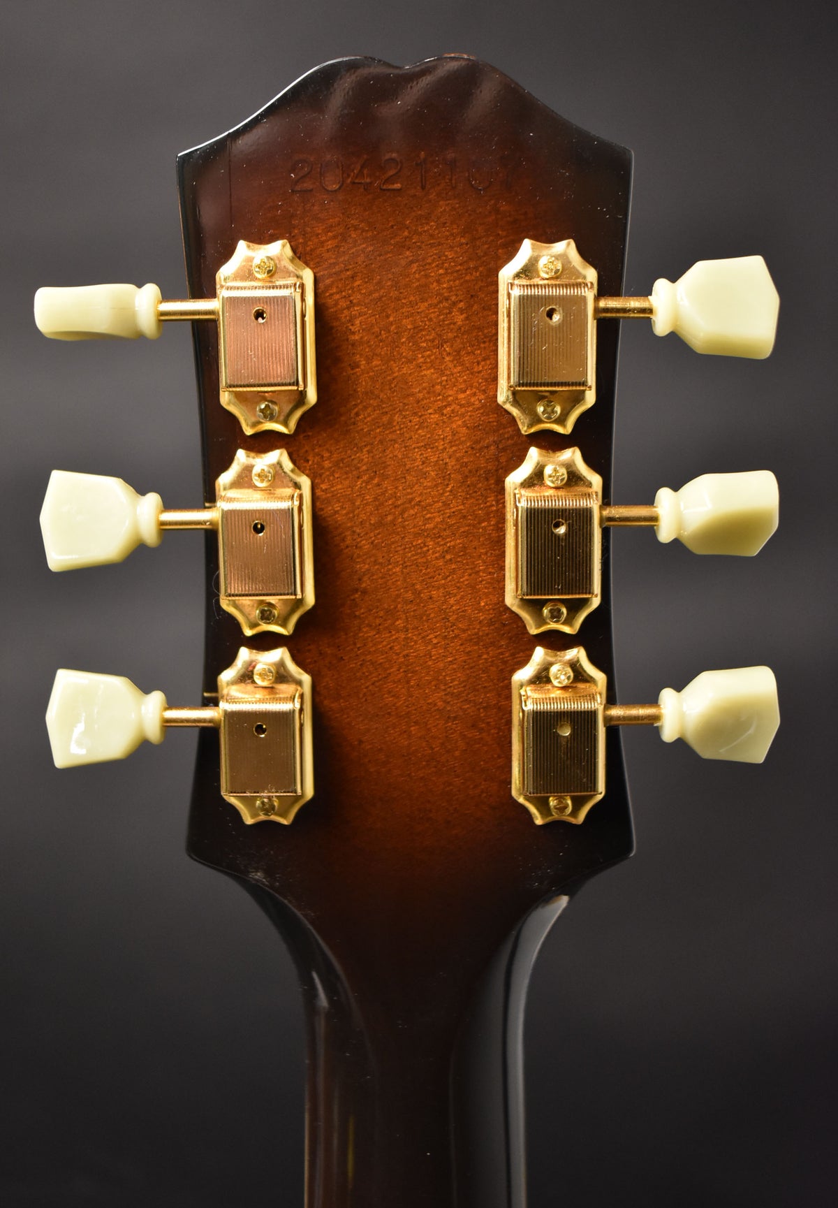 The guitar's headstock, viewed from the back, shows a sunburst finish with six gold-plated tuners and cream buttons.