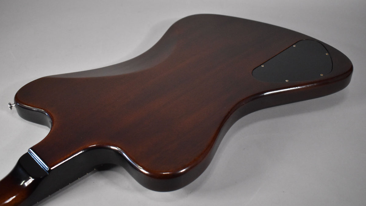 The guitar's dark brown back is angled, showing a black control cavity cover and a chrome strap button near the neck joint.