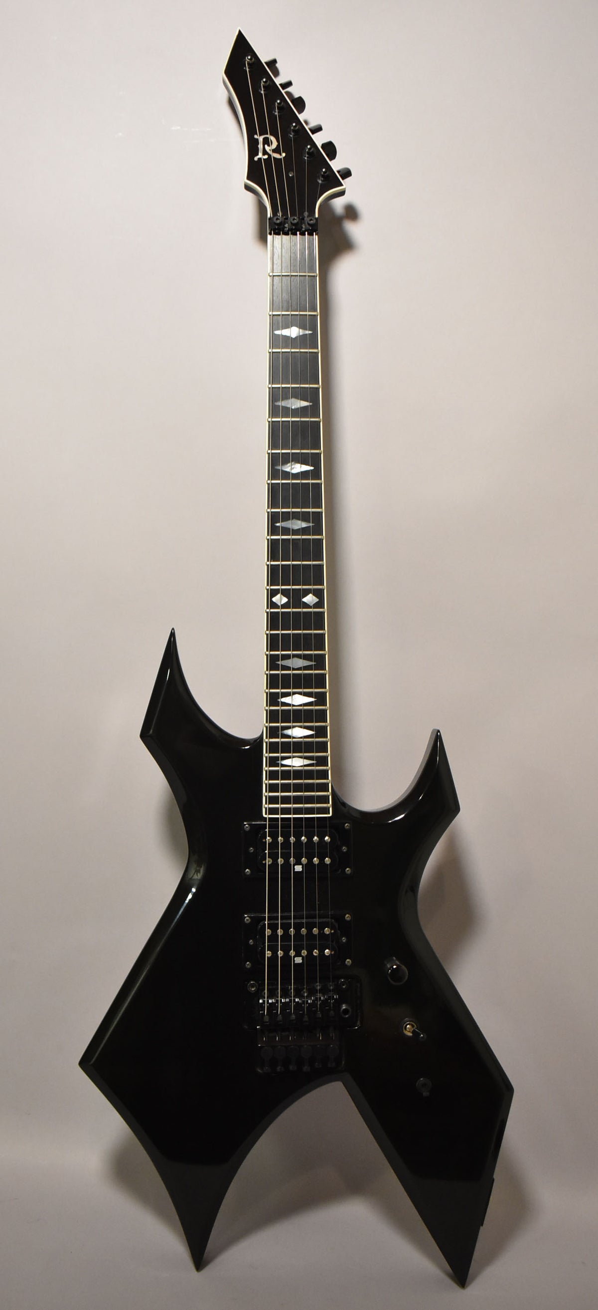 Full-length, front view of a glossy black electric guitar with a pointed headstock, diamond inlays, and black hardware.