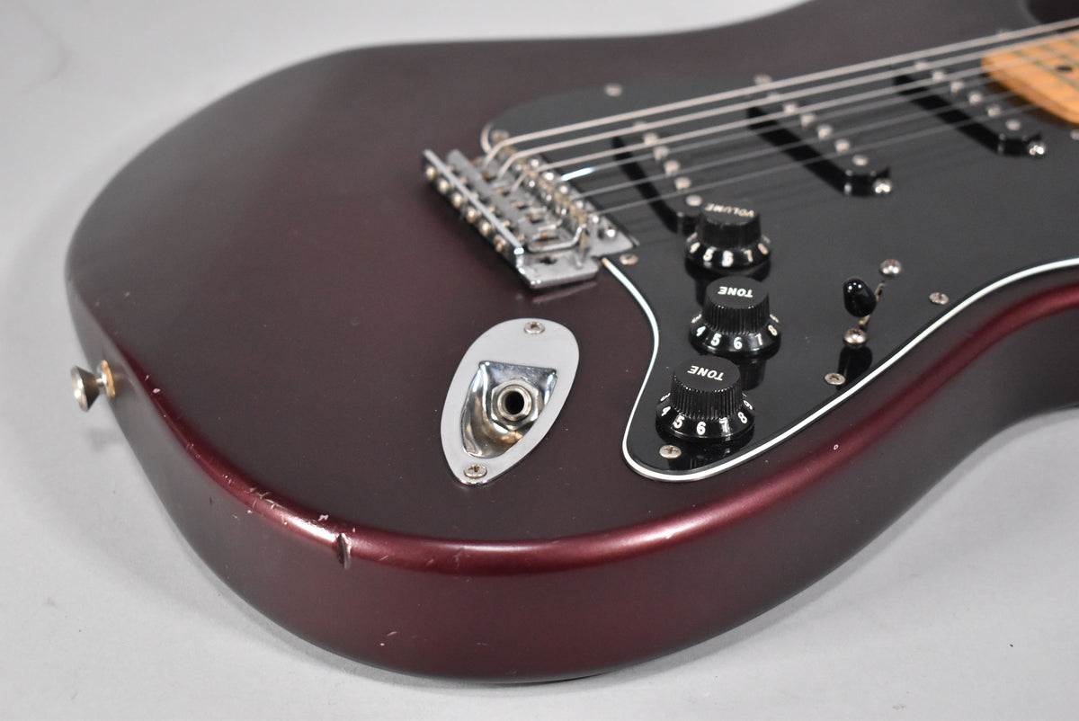 Close-up of the lower body, showing the satin metallic red finish, black pickguard, controls, and wear around the input jack.