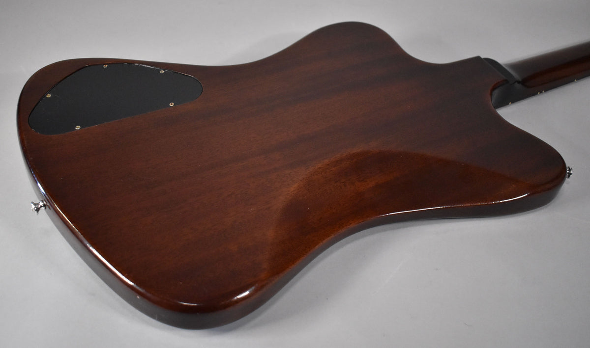 The back of a glossy, dark brown Firebird guitar, angled from the lower left, showing a black control plate and strap buttons.