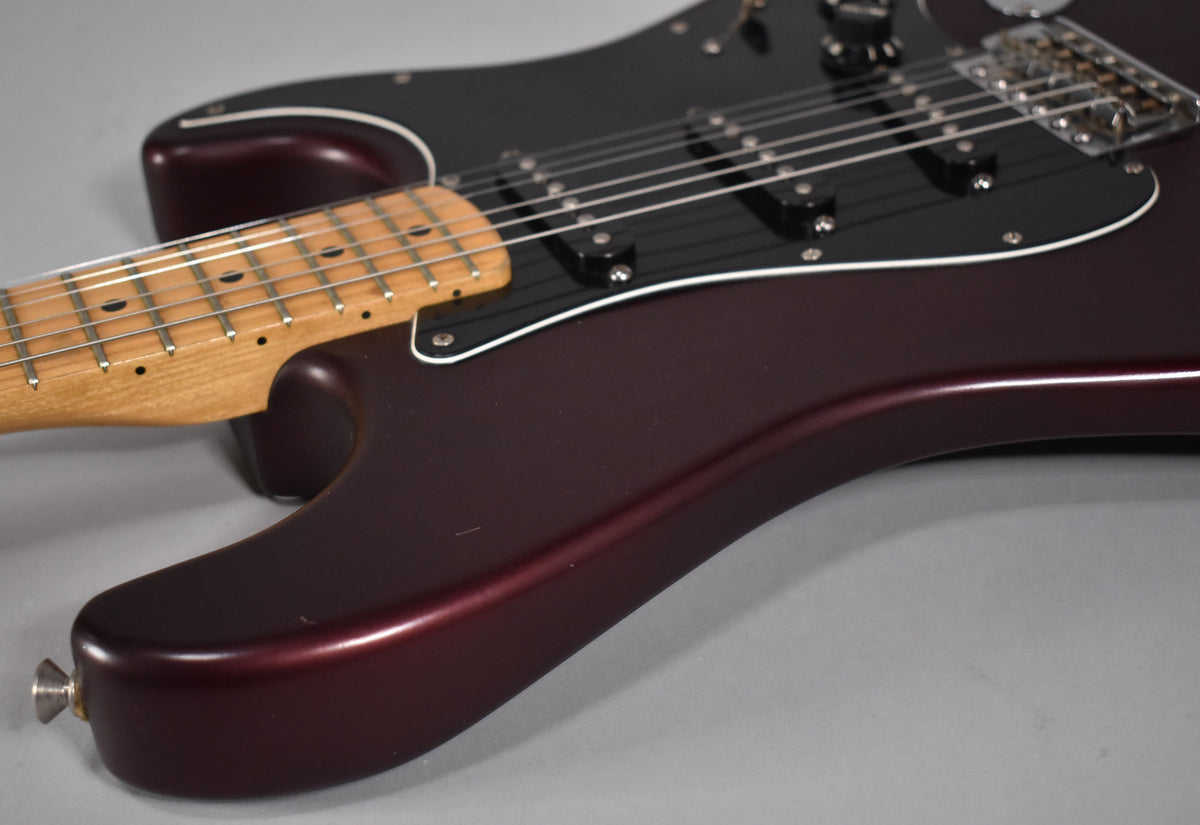 Close-up of the lower body of a metallic red Stratocaster, showing the black pickguard, three single-coil pickups, and maple neck.