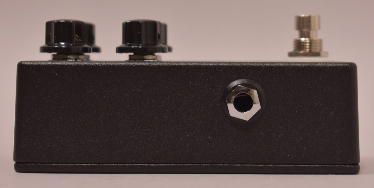 Side view of the black textured pedal, showing two black control knobs, a chrome input jack, and a chrome footswitch.