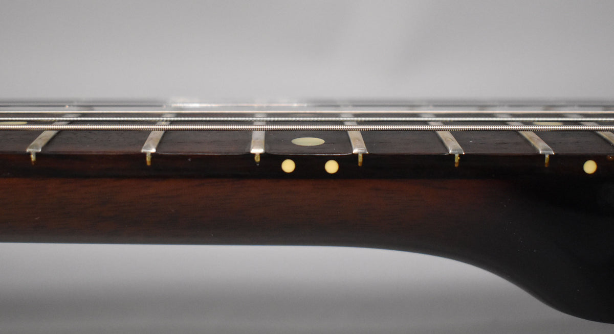 Close-up of the dark rosewood fretboard with frets, strings, and cream dot inlays, showing the neck's curve.