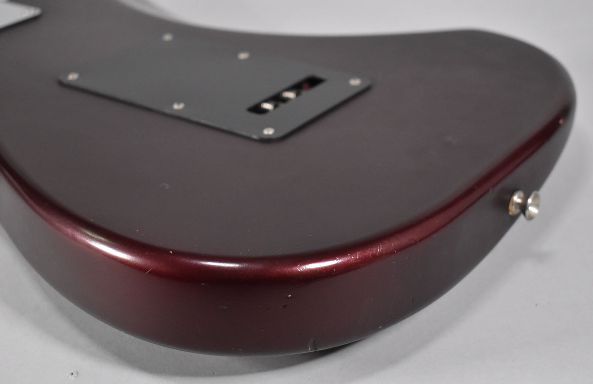 The lower bout of a satin metallic red Stratocaster, showing a black tremolo cover and strap button, with visible wear on the edge.