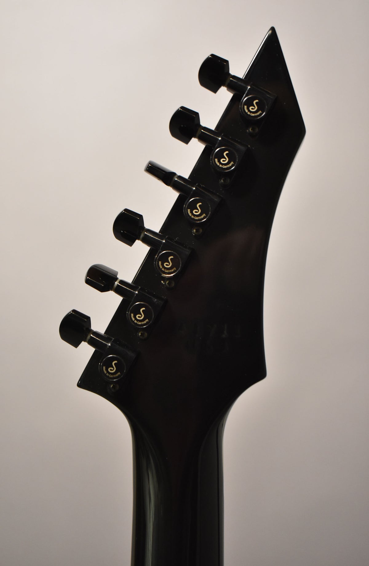The guitar's black headstock, angled left, features six black tuning pegs with gold "S" logos, and a faint serial number.