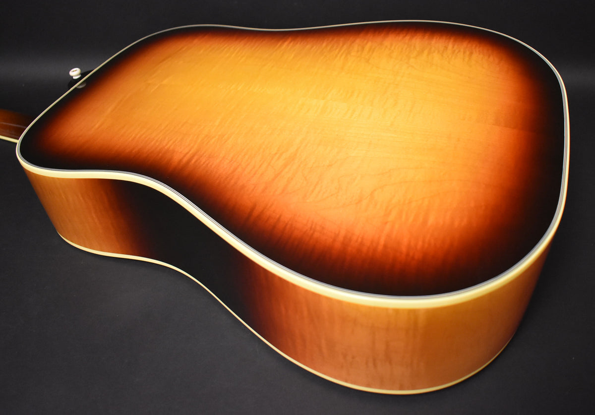The guitar's sunburst back and side are visible, with a subtle flame maple pattern and cream binding along the edges.