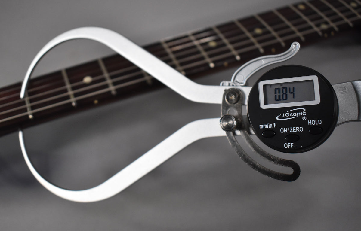 A digital caliper measures the dark rosewood fretboard, showing 0.84 on its screen, with dot inlays visible.