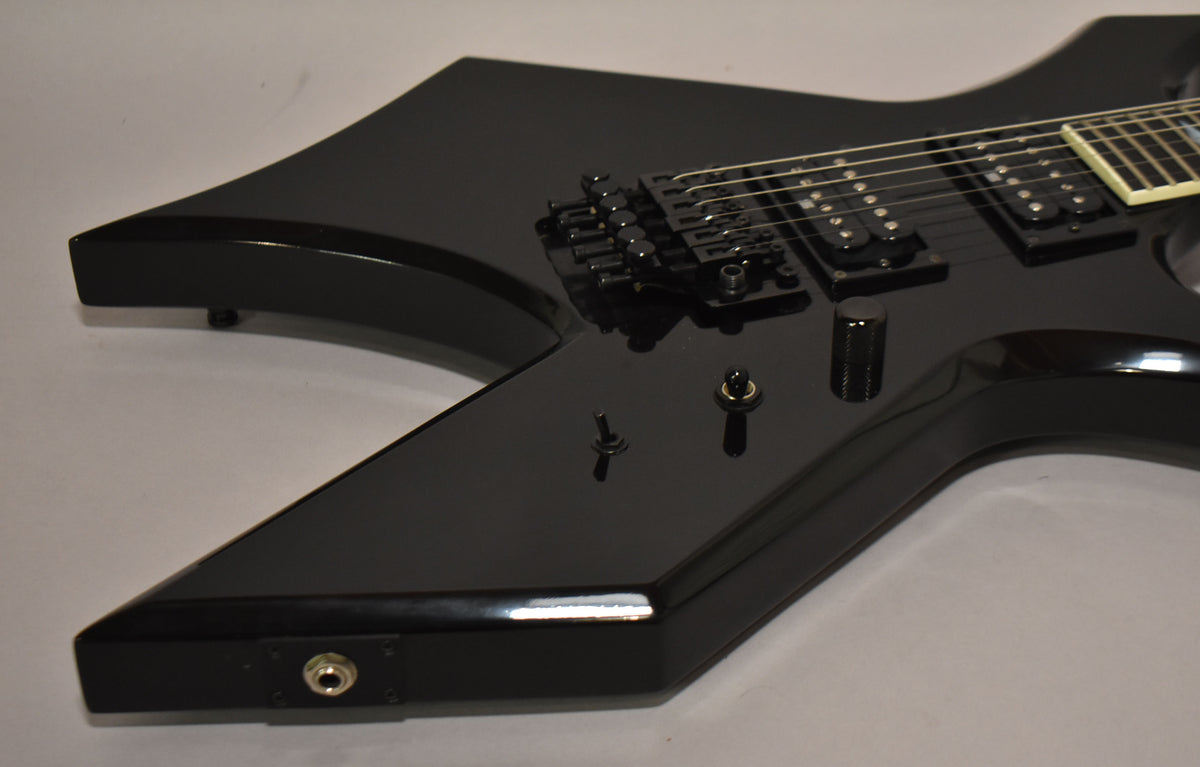 The black gloss Warlock body, angled from the lower bout, shows two humbuckers, a Floyd Rose bridge, and three control knobs.
