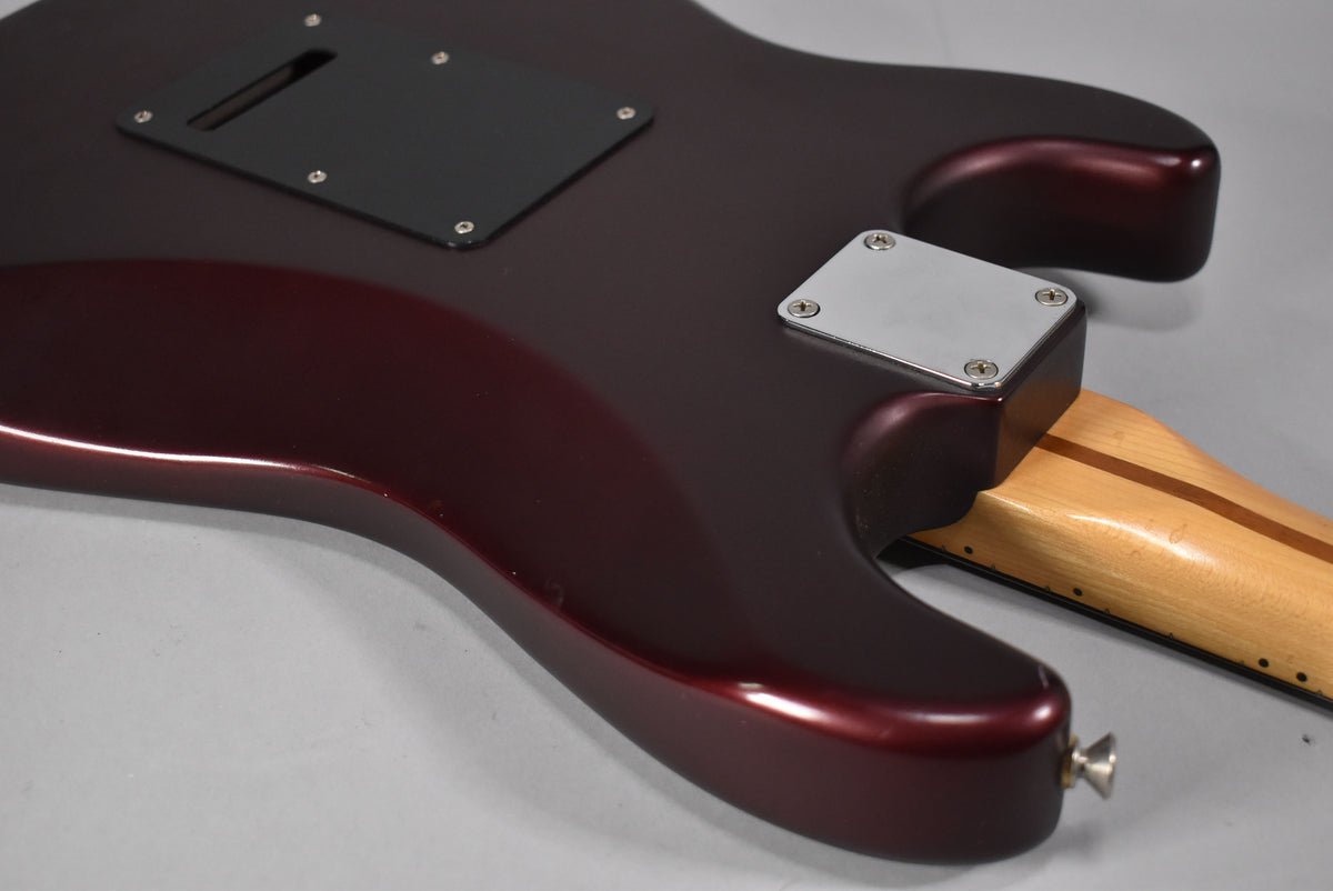The back of the metallic red guitar body, showing the neck joint, black tremolo cover, and a few small dings on the lower bout.