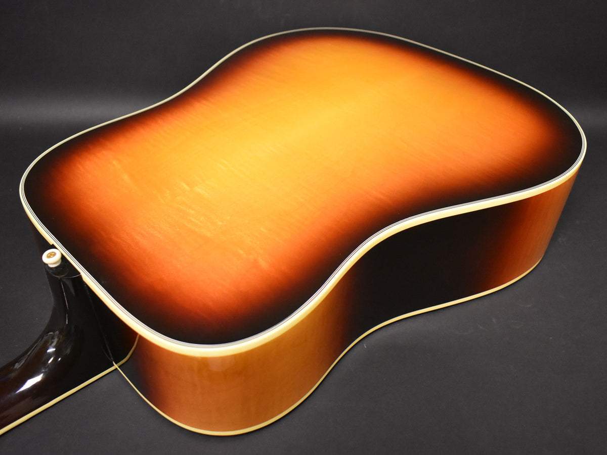 The back of the sunburst acoustic guitar, showing a glossy finish, light wood grain, and cream binding around the body.