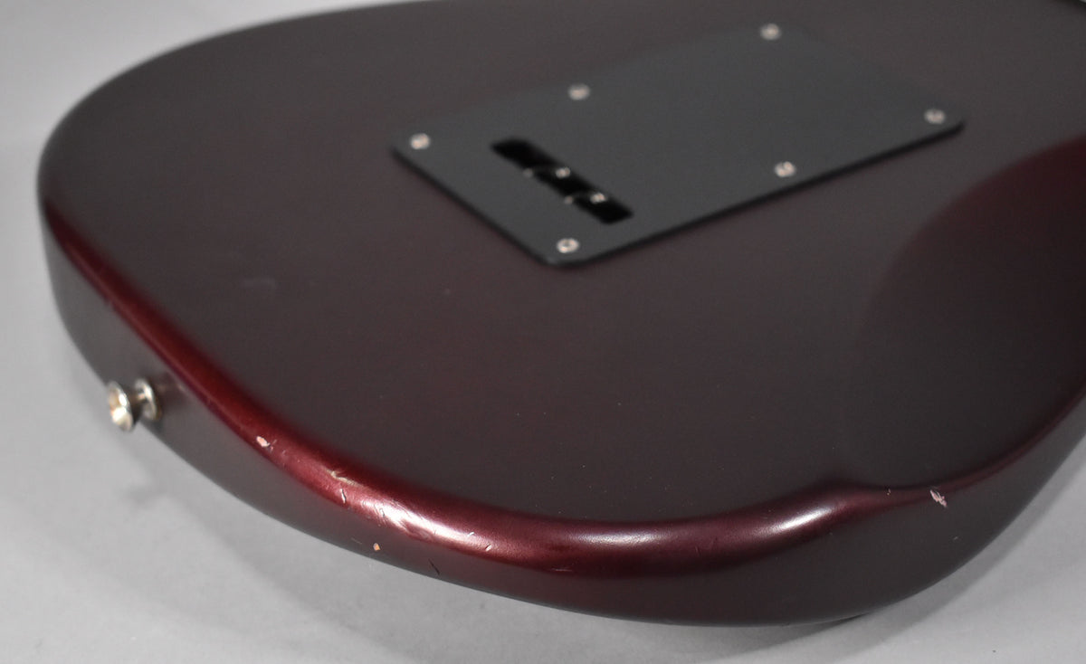 The lower bout of the metallic red satin guitar body, showing the black tremolo cover and wear along the bottom edge.