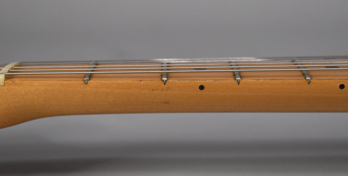 Close-up of the guitar's light brown maple neck and fretboard, showing the nut, frets, strings, and a black dot inlay.