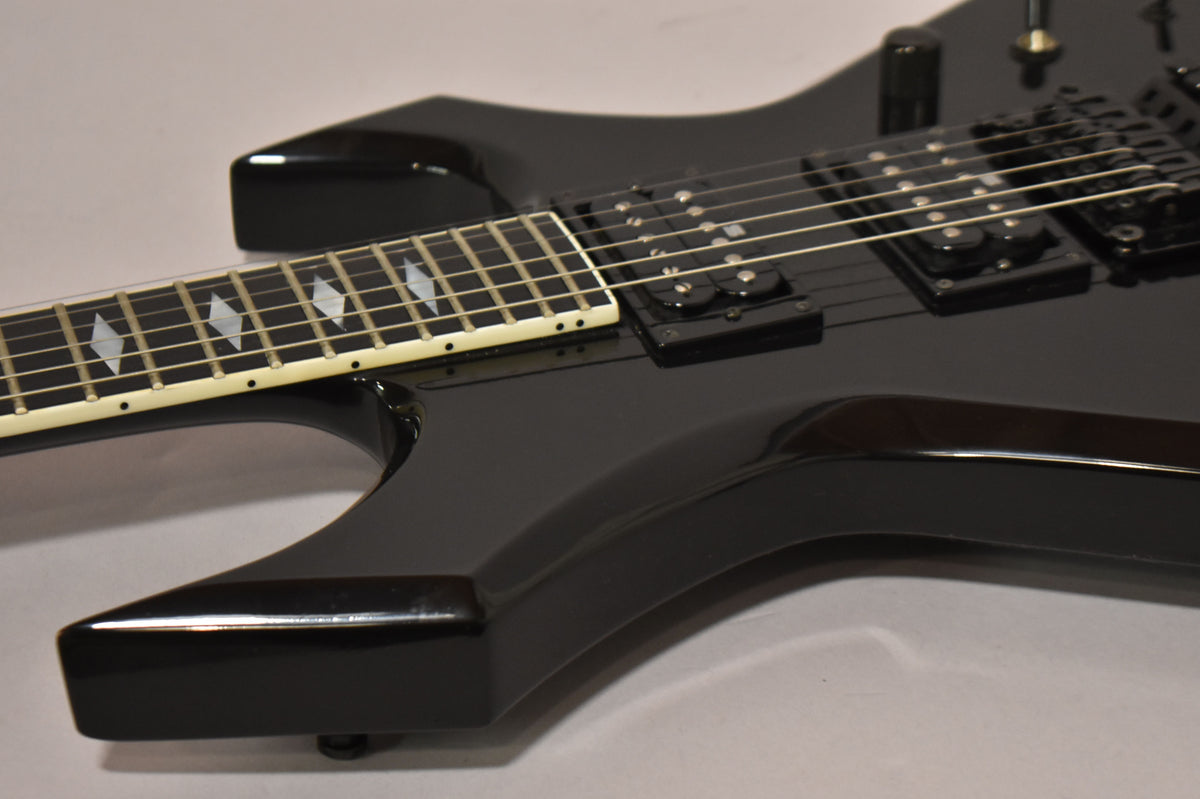 Close-up of the glossy black body and fretboard with diamond inlays, showing two humbucker pickups and a volume knob.