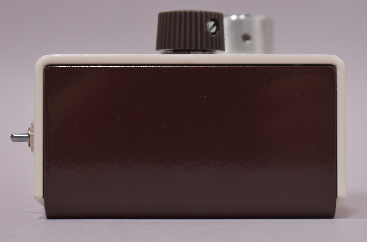 The pedal's right side is shown, with a glossy dark brown finish, a small silver toggle switch, and two control knobs on top.