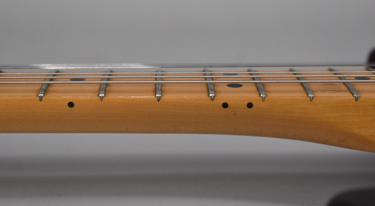 Close-up of the maple fretboard and frets, showing black dot inlays and some minor wear on the wood.