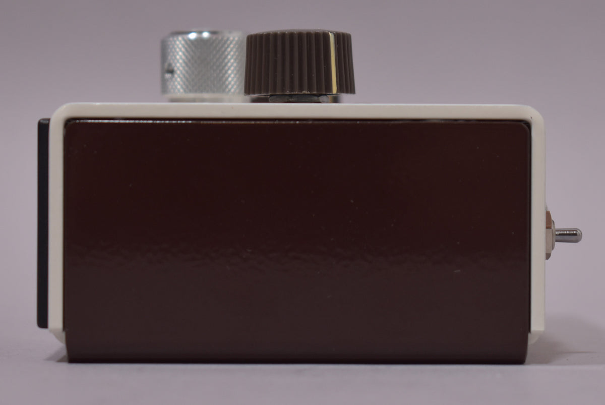 The pedal's right side, showing its glossy dark brown body, cream top edge, and a silver toggle switch on the far right.
