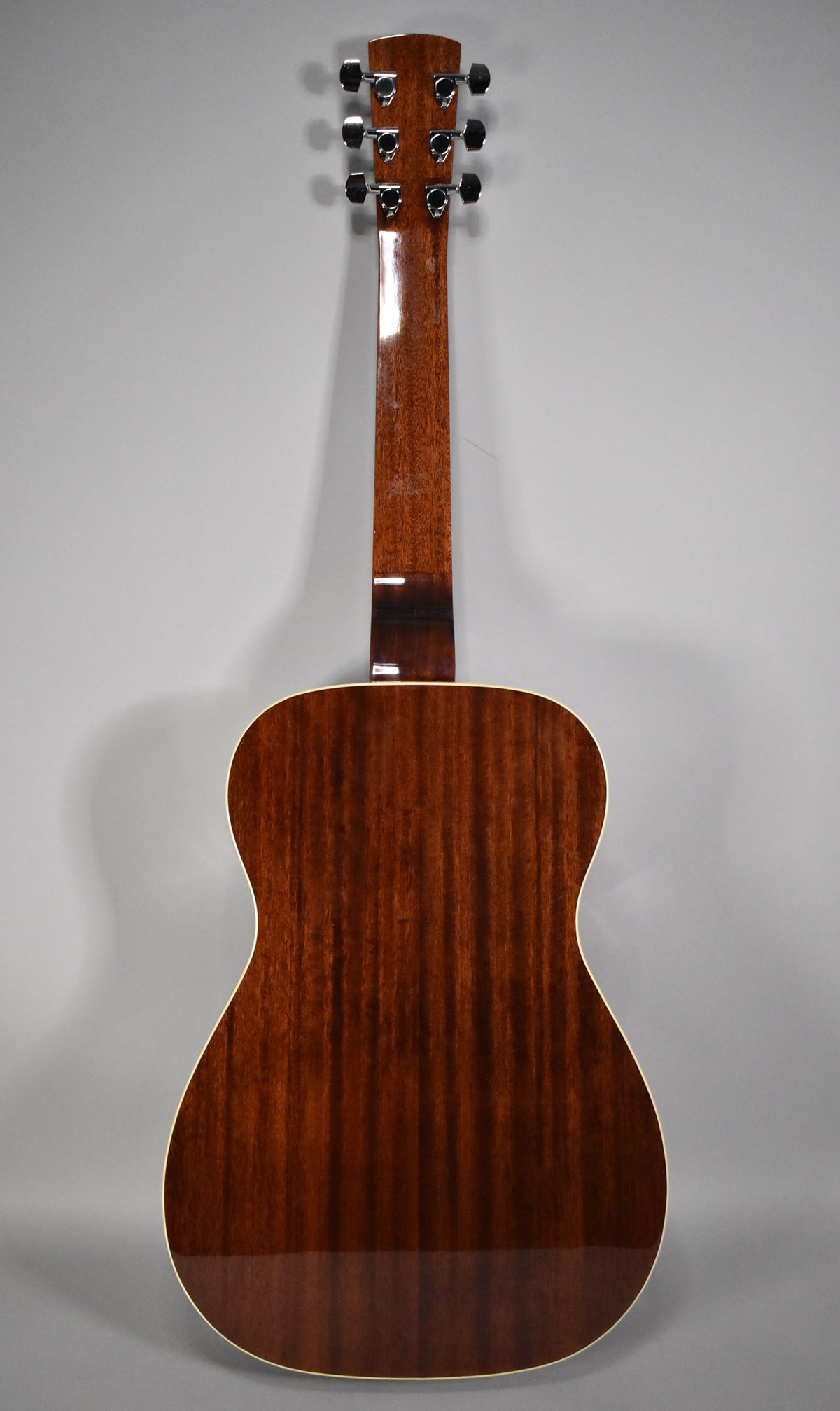 Full rear view of the guitar, showing a dark reddish-brown body with vertical grain and a glossy finish, and six chrome tuners.