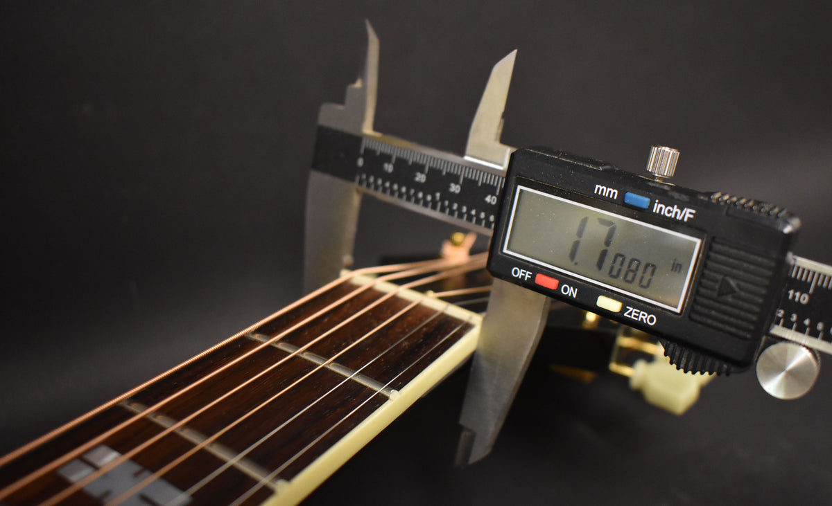 A digital caliper measures the guitar's nut width at 1.7080 inches, with the dark fretboard and light binding visible.