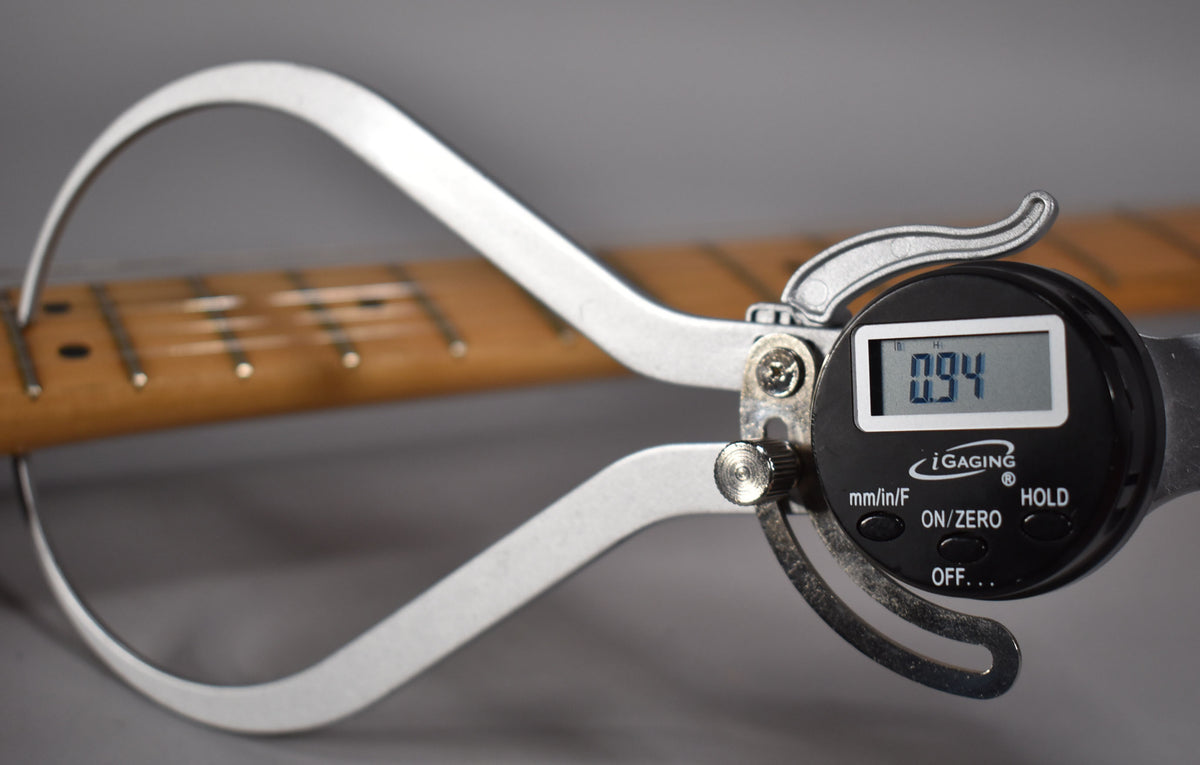 A digital caliper measures the neck thickness at the first fret, displaying "0.94" on its screen.